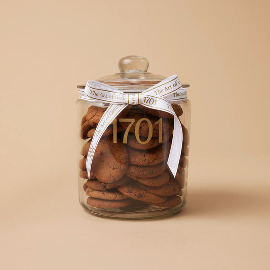A 1kg glass jar of handmade biscuits with chocolate chips, presented in a glass jar with a hand-tied signature ribbon on a warm background, with the product label visible on the front of the jar. The biscuits are SANHA Halaal approved, making them a perfect gift idea for anyone who appreciates high-quality biscuits made with care.