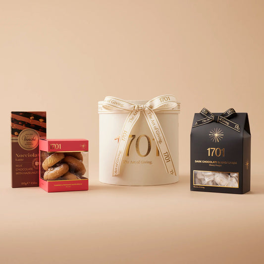 A warm background showcases the "Care & Connection" gift box, featuring a box of handcrafted honey nougat, a box of delicious biscuits, and a slab of imported chocolate. The product label is visible on the front of the box. The gift box is a thoughtful gesture to show someone they are on your mind and that you care for them.