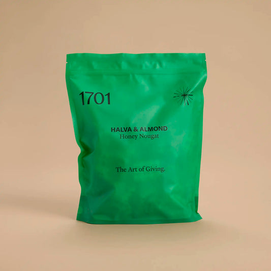 1 kg pouch of Halva & Almond honey nougat, shown in a dark green pouch on a warm background. The pouch is filled with bite-sized pieces of nougat, and the product label is visible on the front of the pouch.
