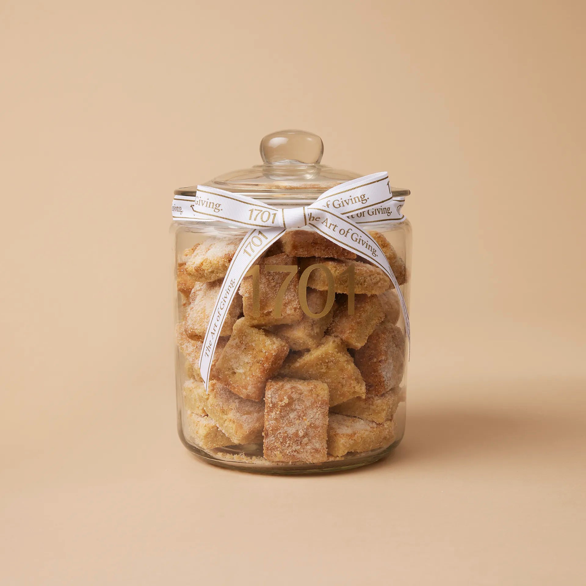 A 1kg glass jar of handmade biscuits with macadamia nuts and nougat, presented in a glass jar with a hand-tied signature ribbon on a warm background, with the product label visible on the front of the jar. The biscuits are SANHA Halaal approved, making them a perfect gift idea for anyone who appreciates high-quality biscuits made with care..