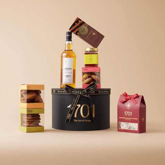 A gift box with a bottle of anCnoc 12 year old single malt Scotch whisky, a box of handcrafted honey nougat, a selection of biscuits, and a jar of farm honey, all presented in a signature hat box. Perfect for whisky lovers and those who appreciate high-quality treats.