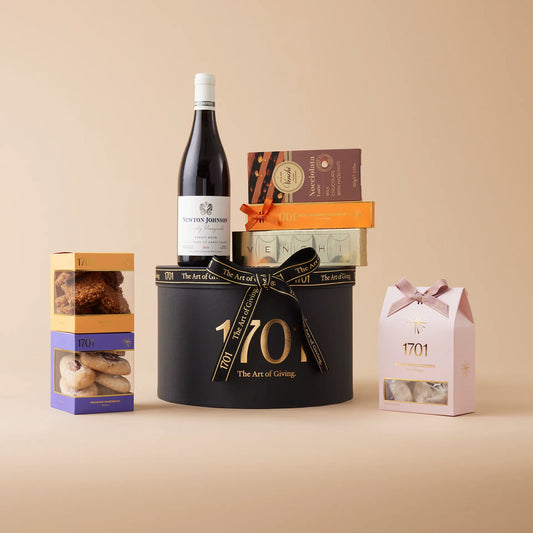 A luxurious gift box filled with treats for wine and dessert lovers. It includes a box of handcrafted honey nougat, two boxes of biscuits, and two imported Italian chocolates by Venchi, all presented in a stylish box with a ribbon. The centerpiece is a bottle of Newton Johnson Family Vineyards 2020 Pinot Noir or 2020 Chardonnay, making it the perfect gift for anyone who enjoys a good wine and gourmet snacks.