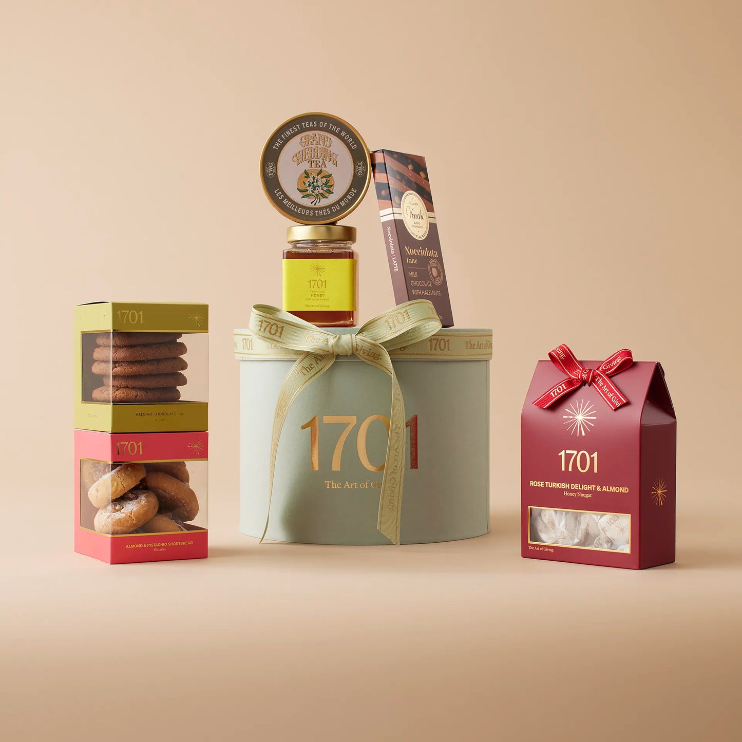 The Terrific Teatime Gift Box is presented on a warm background. The gift box includes a box of handcrafted honey nougat, two boxes of biscuits, a jar of farm honey, an imported Italian chocolate, and a stunning tin of TWG tea. This gift box is designed for sharing a perfect cup of tea with a close friend, indulging in the luxury of fine treats. The green and gold design of the gift box adds a touch of elegance to this special gift, making it perfect for any occasion or just because.