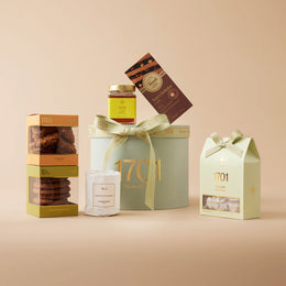 The Aromatic Gift Box. A box filled with a variety of items, including a box of handcrafted honey nougat, two boxes of biscuits, a jar of honey, an imported chocolate by Venchi, and a scented candle from De Nagmaal. A perfect gift to indulge the senses.